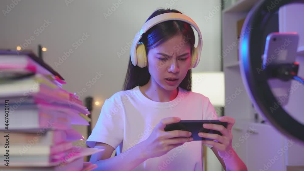Excited Young Asian woman wearing headset and playing online game on smartphone with live broadcasting on internet. Excited Young Asian woman wearing headset and playing online game on smartphone with live broadcasting on internet.