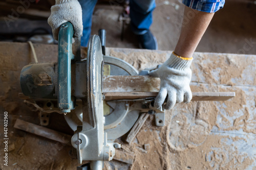 Fototapeta Naklejka Na Ścianę i Meble -  Top view of hands of male carpenter wearing safety gloves at work. woodworker using circular saw cutting piece of wood at woodwork workshop