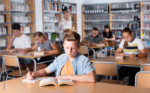 Diligent serious positive schoolboy preparing for lesson with books in school library indoor