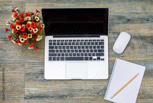 Top view of laptop  computer with paper notebook and white mouse and fake flower pot on wooden pattern background with copy space