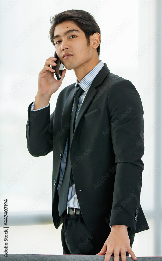 Closeup handsome young Asian businessman wearing formal suit, showing happy expression, smiling with confidence while talking mobile phone, presenting about technology and convenient communication. Closeup handsome young Asian businessman wearing formal suit, showing happy expression, smiling with confidence while talking mobile phone, presenting about technology and convenient communication.