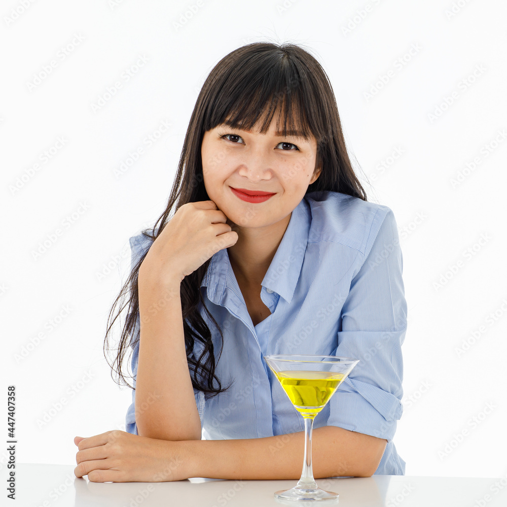 Portrait of top half asian girl with long straight hair, red lips and hands touching the chin, arms resting on a table. There is yellow cocktail in front of and white background. Portrait of top half asian girl with long straight hair, red lips and hands touching the chin, arms resting on a table. There is yellow cocktail in front of and white background.