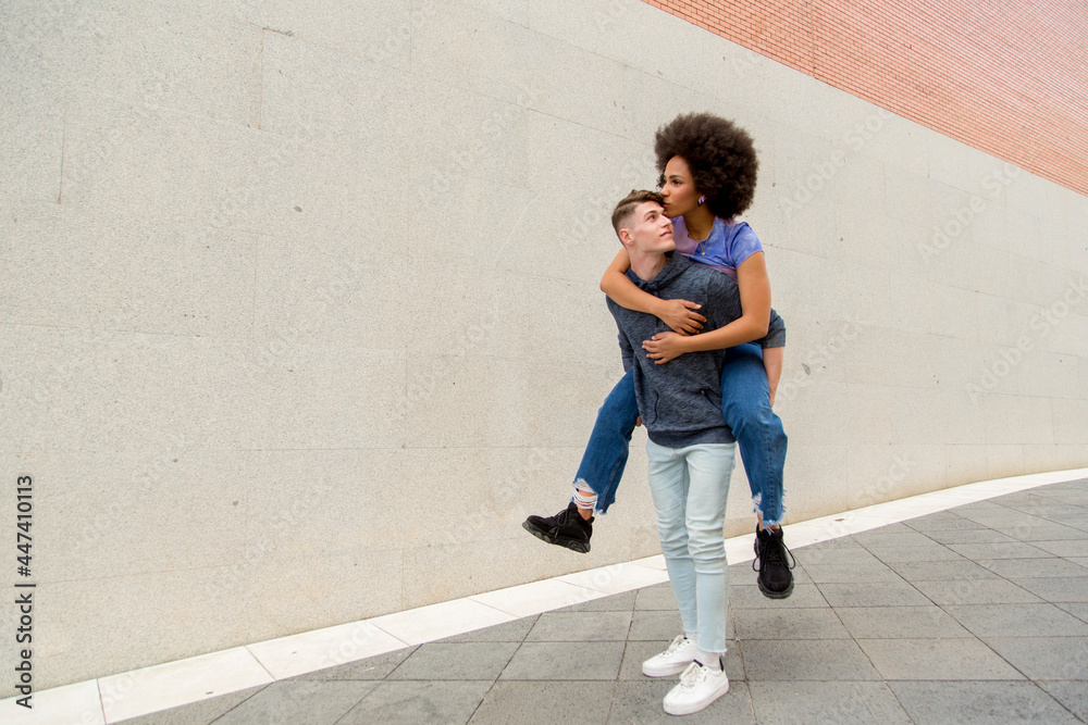 multiethnic couple Caucasian young man carrying afro woman on his back giving his a kiss multiethnic couple Caucasian young man carrying afro woman on his back giving his a kiss