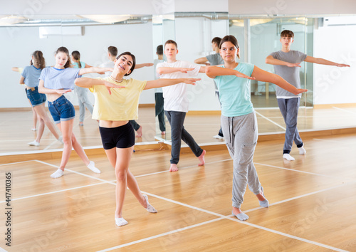 Diligent friendly smiling teenagers learn dance movements in dance class