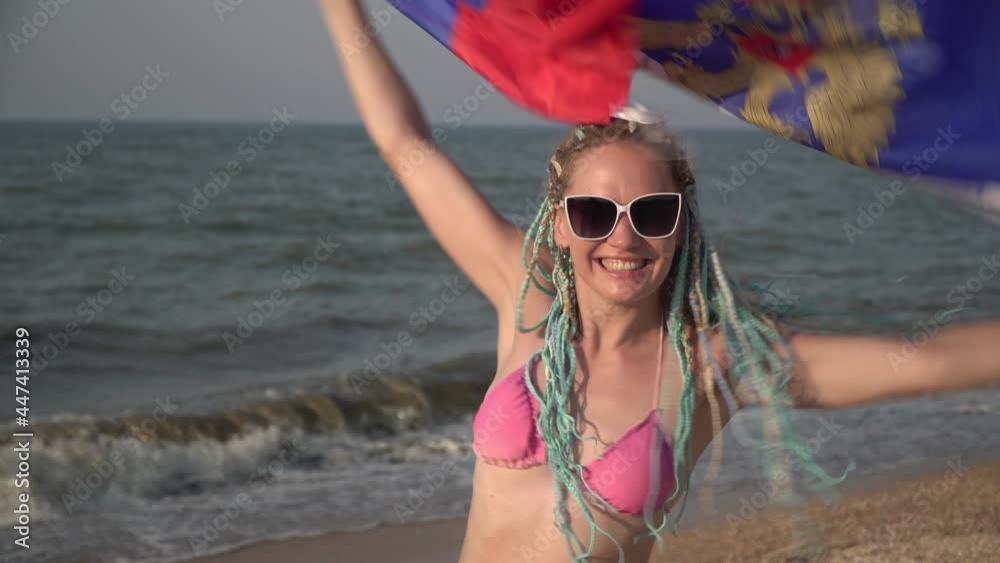Beautiful woman with the flag of Russia at the sea. Happy woman tourist with Russian flag on the beach