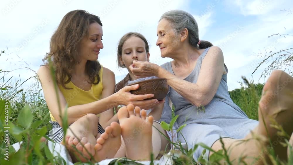 Cute child girl with her young mother and senior grandmother are having picnic during summer outdoor in nature, mothers day, happy retirement, multi generation family