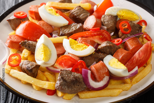 Bolivian Pique A Lo Macho is a dish prepared with cooked meat and sausage served over fries and garnished with vegetables, eggs closeup in the plate on the table. Horizontal photo