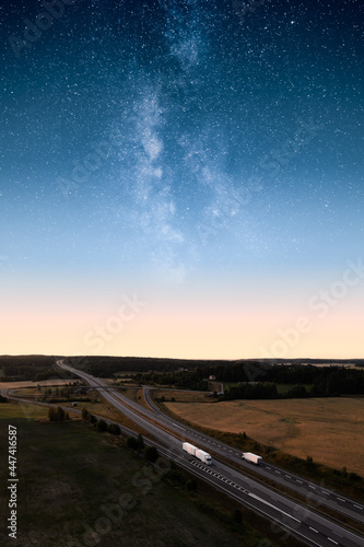 Truck on a highway with an epic milky way and stars sky above. Transportation and cargo at night.
