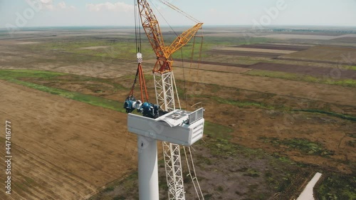 Wind generator installation. Powerful truck crane installs electric rotor into generator container standing on wind farm among green brown fields aerial view