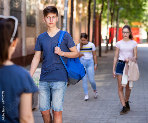 Modern teenager dressed in blue tee shirt and denim shorts walking along city street on summer day