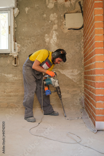 Young builder breaking up a house floor with a jackhammer.