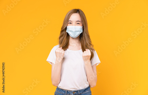Asian woman wear masks to protect disease and with fists clenched celebrating victory expressing success on yellow background.