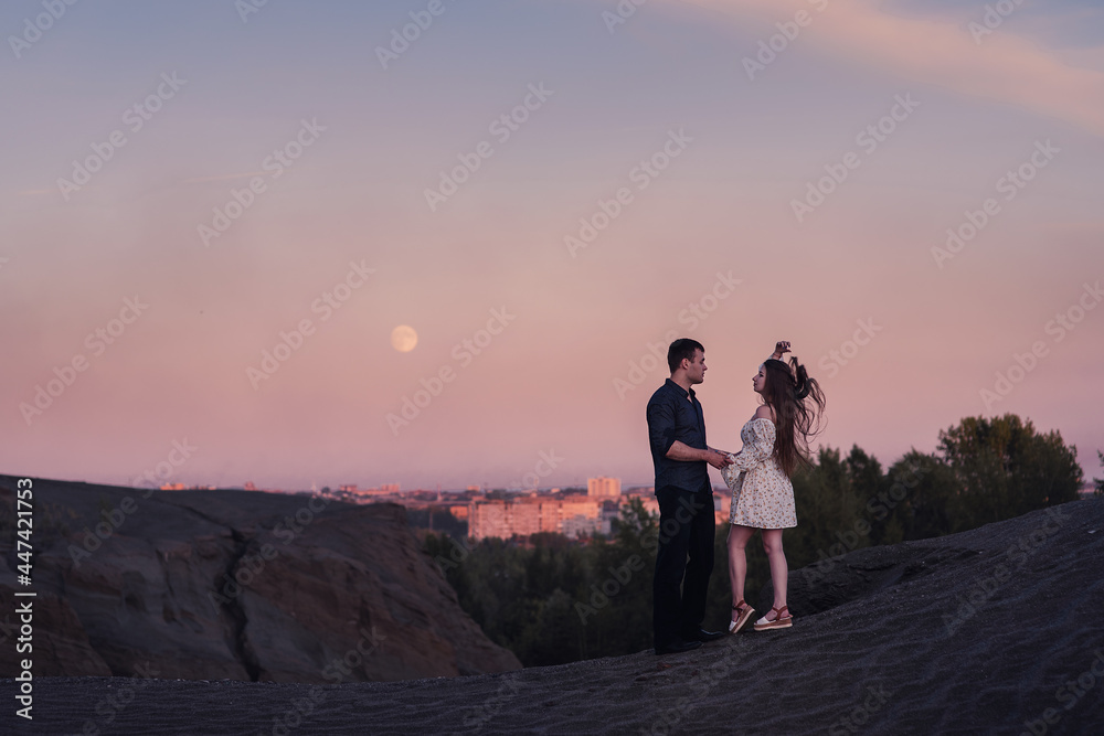 Loving couple embracing and looking moon and city oin sunset