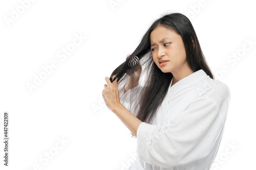 a woman wearing a towel is annoyed that her hair is tangled when it is combed against a light gray background