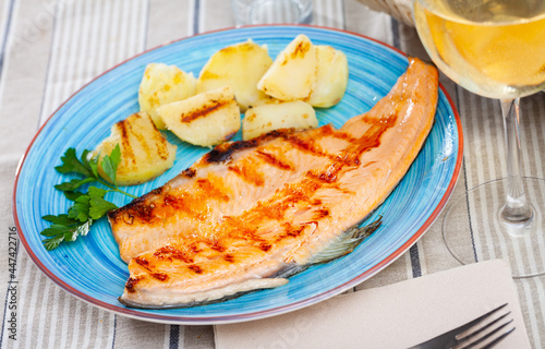 Appetizing roasted trout fillet with baked potatoes served with glass of white wine