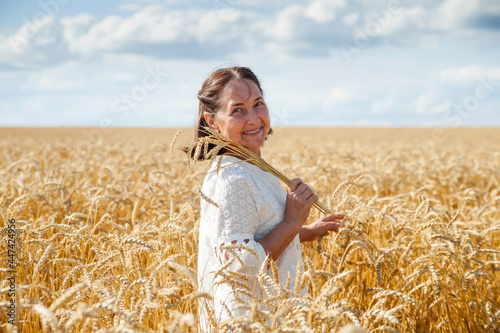 Beautiful mature woman in white on   background of   blue sky and   wheat field © DariaTrofimova