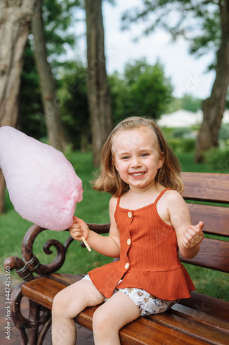 Beautiful little girl eating pink cotton candy in the park.