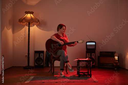 Woman playing acoustic guitar in a retro vintage room.