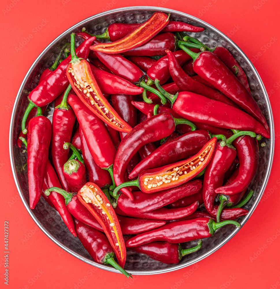 Fresh red chilli peppers in the metal plate isolated on red background.