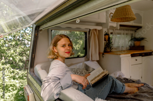 Konstfotografi young lady reading a book at a campervan in the nature, glamping, recovery
