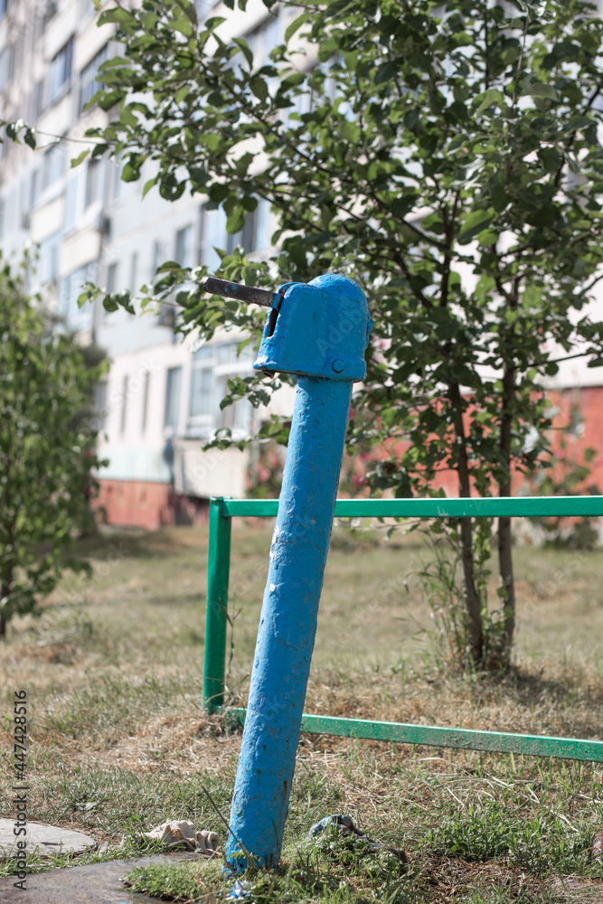 A blue street water pump in a modern city against the backdrop of a nine-story Soviet building A blue street water pump in a modern city against the backdrop of a nine-story Soviet building