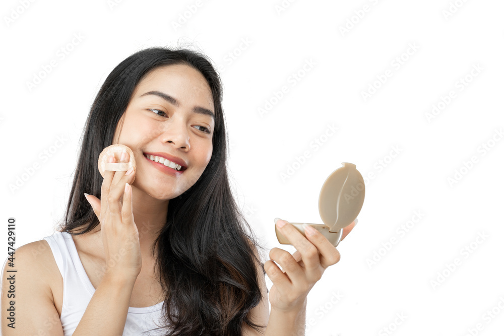 young beautiful woman with long black hair using puff to wipe powder on cheeks while holding small mirror on gray background young beautiful woman with long black hair using puff to wipe powder on cheeks while holding small mirror on gray background