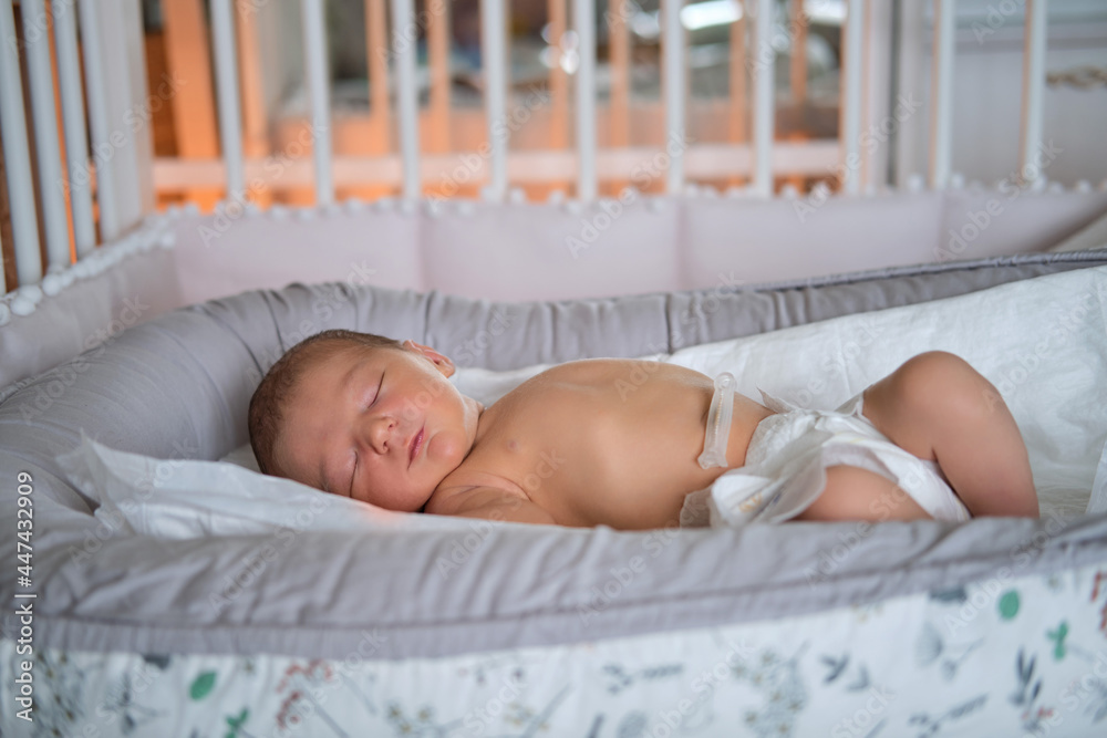 A baby boy sleeps in a cocoon on a cot. A newborn baby in a diaper is