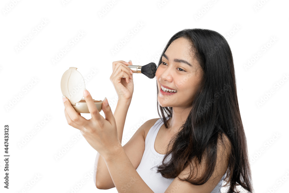 asian woman with long black hair using brush to wipe powder on cheeks while looking at small mirror on gray background asian woman with long black hair using brush to wipe powder on cheeks while looking at small mirror on gray background