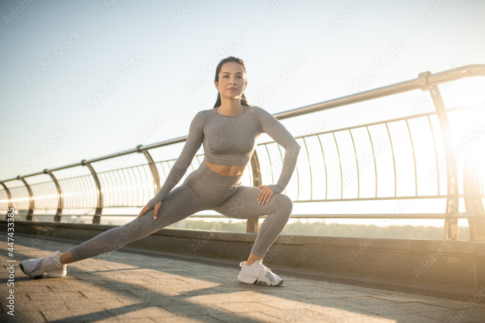 Cute girl in grey sportswear stretching her legs in lunges