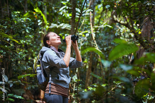 Smiling woman tourist watching birds with binoculars in the rain forest