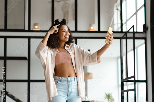 Black young woman gesturing while taking selfie on mobile phone