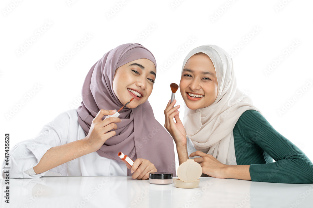 Two young girls in veil making a video for their blog when testing new lipstick product against white background