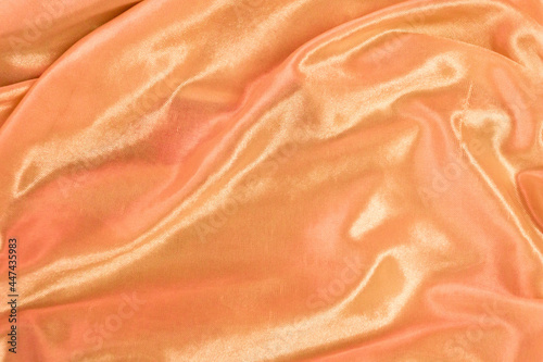 Rippled orange silk fabric background. Closeup of redish drapery cloth or satin, luxury, and elegant light orange texture 