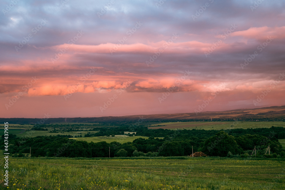 scarlet and lilac storm clouds at sunset and a green meadow