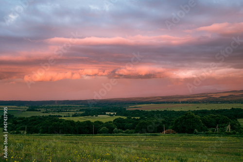 scarlet and lilac storm clouds at sunset and a green meadow