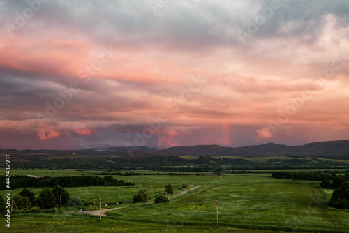 pink and lilac storm clouds at sunset and a green meadow