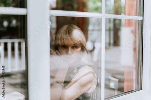 Senior woman sits in front of the window. Mature adult woman looking sad and thoughtful. Mental health and depression.
