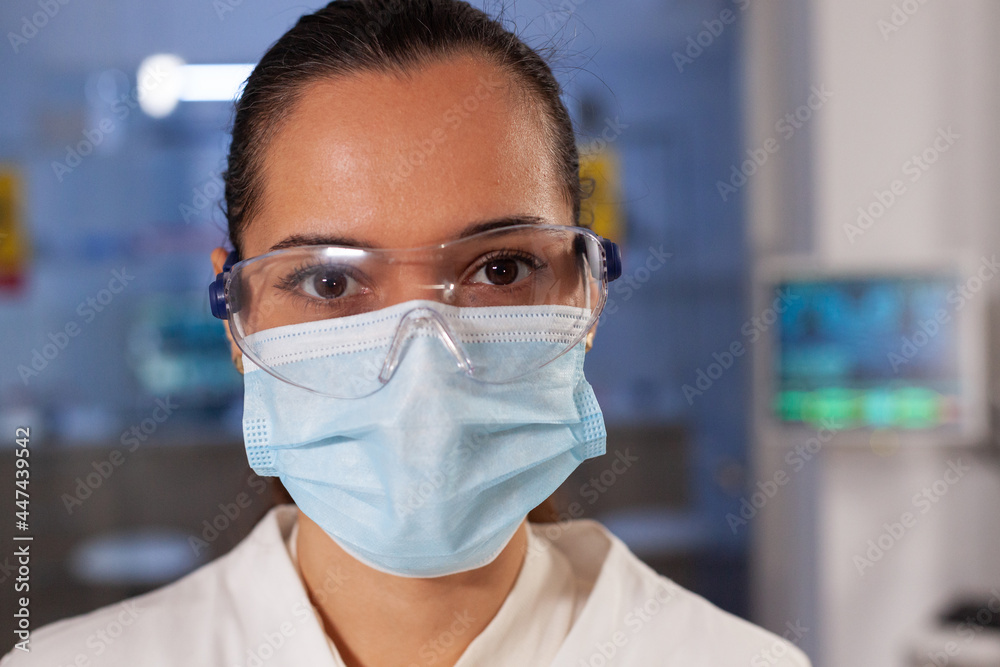 Portrait of biotechnology chemist working in laboratory at medical hospital. Woman with scientist occupation wearing protection glasses, face mask and lab coat industry equipment Portrait of biotechnology chemist working in laboratory at medical hospital. Woman with scientist occupation wearing protection glasses, face mask and lab coat industry equipment