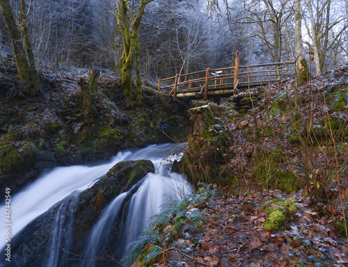 late autumn scene with a tall waterfall, hand carved wooden bridge and mossy trees somewhere in the west german woods in the region Eifel photo