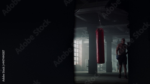 Man finishing boxing training. Boxer walking in loft building with punching bag