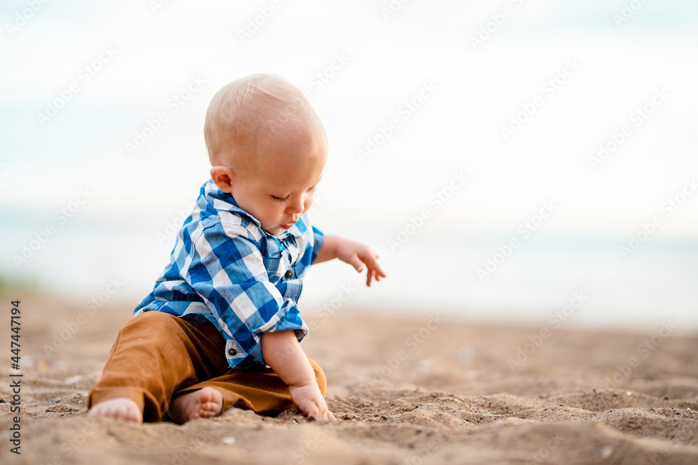 Cute baby boy sitting on the sand on the beach at sunset Cute baby boy sitting on the sand on the beach at sunset