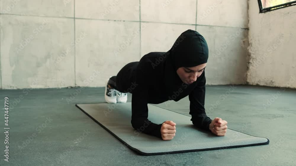 
A concentrated arabian sports woman wearing a national hijab is doing plank exercises in a gym
