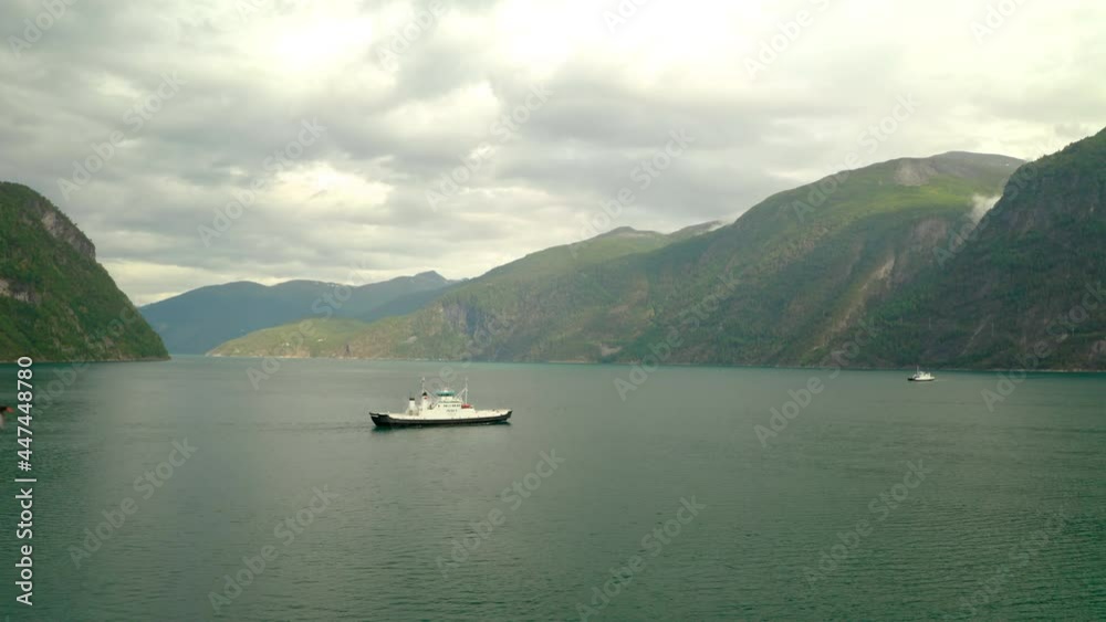 Boat Cruising Across Calm Waters Of Geiranger Fjord In More og Romsdal, Norway With Bird Flying In Foreground. wide aerial Boat Cruising Across Calm Waters Of Geiranger Fjord In More og Romsdal, Norway With Bird Flying In Foreground. wide aerial