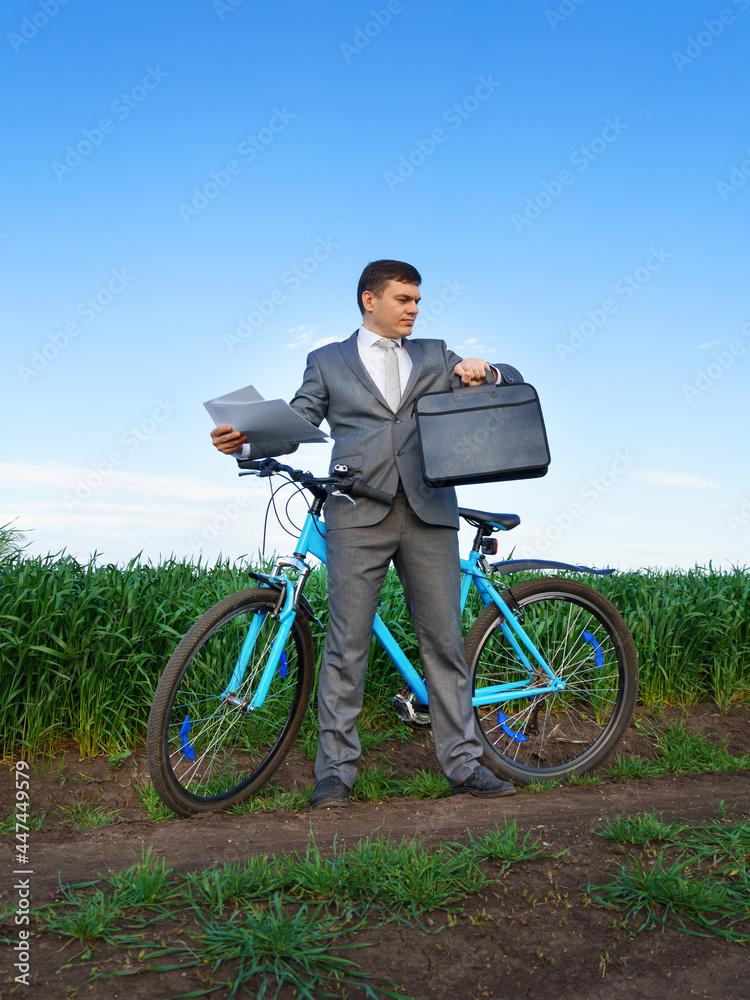 Businessman with a bicycle works with documents in a green grass field - business concept for freedom, vacation or freelance. Beautiful spring nature. Businessman with a bicycle works with documents in a green grass field - business concept for freedom, vacation or freelance. Beautiful spring nature.