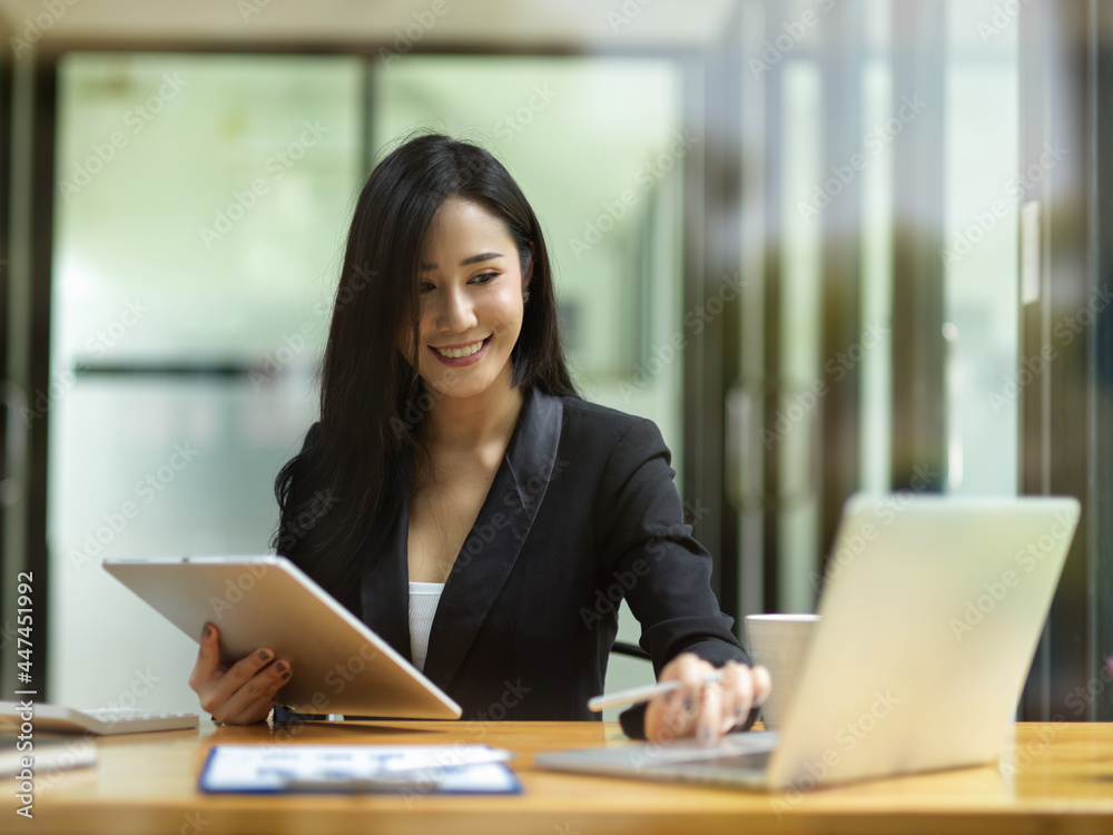 Attractive businesswoman in black suit, using laptop and holding smart tablet Attractive businesswoman in black suit, using laptop and holding smart tablet