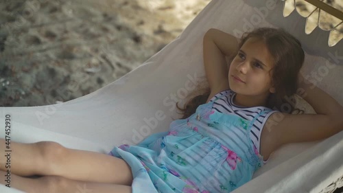Beautiful girl lies in hammock sleeping and dreams. Kid schoolgirl rests in nature with sea beach background