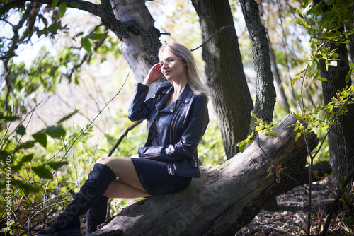 Sexy young woman in a little black dress and biker jacket relaxing in nature