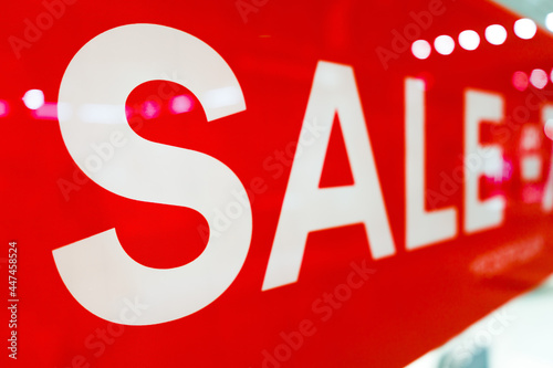 Big white on red SALE close-up advertisement text in showcase window with reflections in store mall