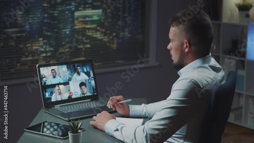 Back view of young multiracial businessman having online meeting with multinational team of young leaders. He sitting at office with skyscrapers in the background.