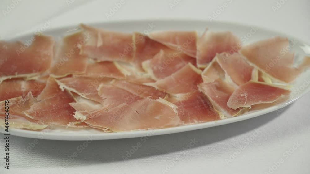 A chef in gloves puts sliced ham on a white plate. Close-up A chef in gloves puts sliced ham on a white plate. Close-up
